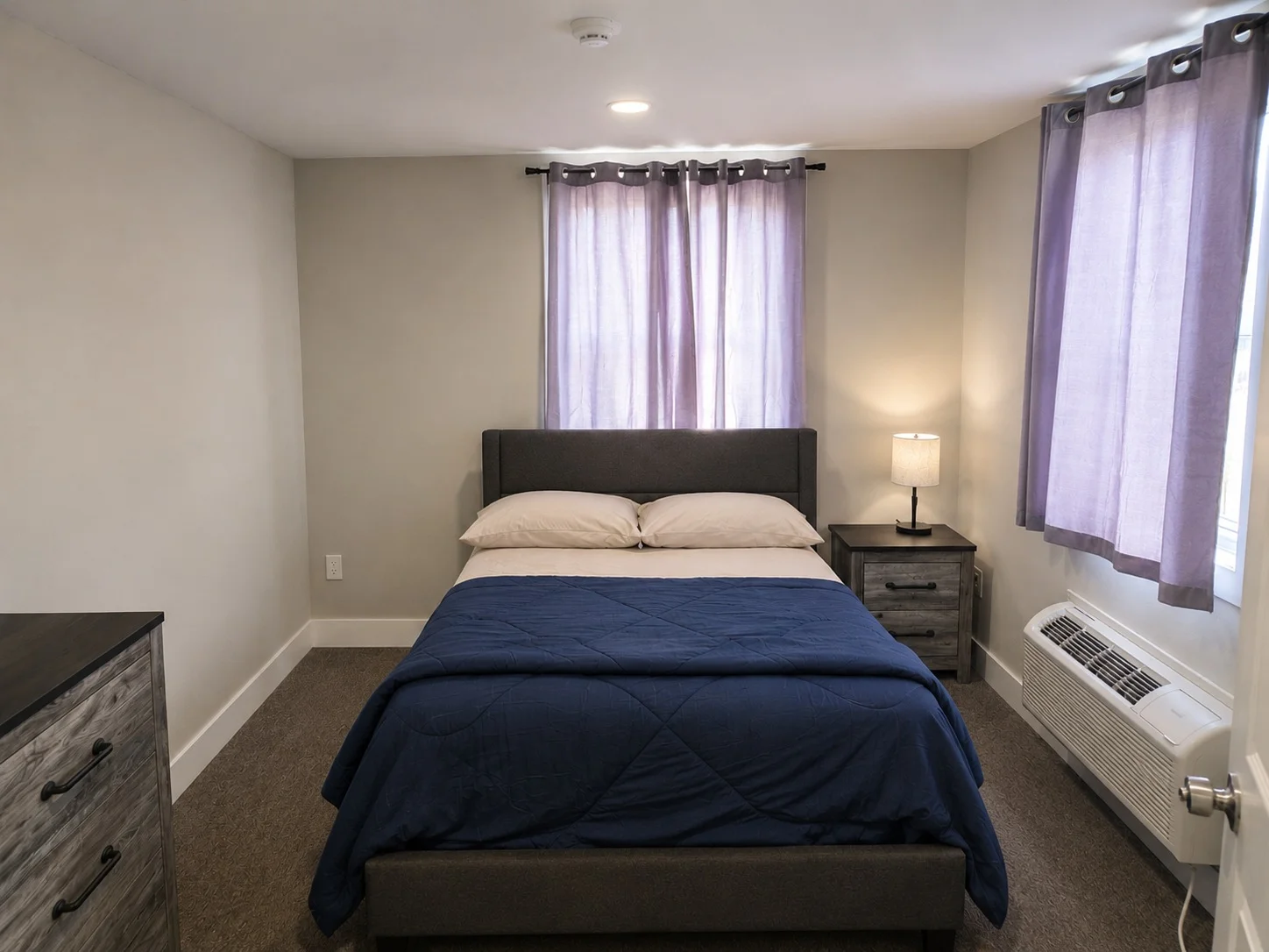 Modern guest room full view with queen bed, windows and dresser